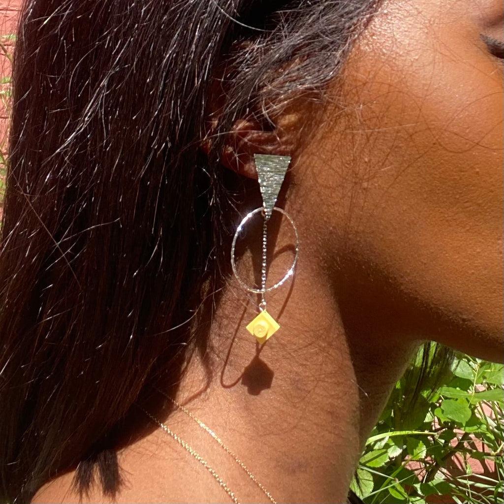 Boucles d'oreilles éthniques argentées avec un triangle martelé à l'oreille d'où sont supendus un cercle martelé et une chaine argentés avec une brique de Lego 1x1 plate jaune pastel